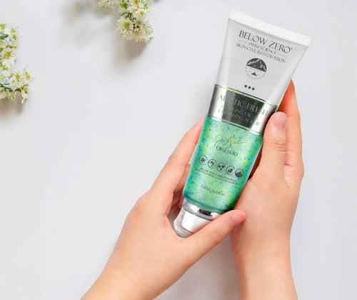 Hands holding Below Zero Arctic Fresh Cooling Facial Cleansing Scrub tube with white flowers