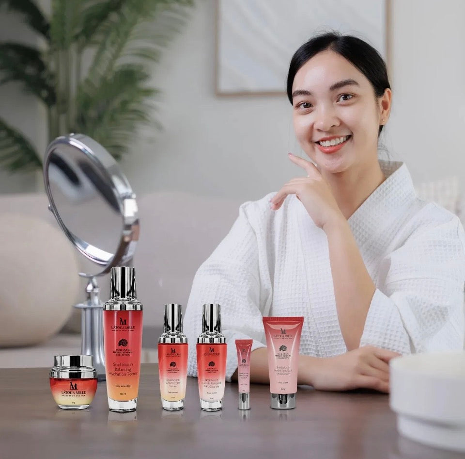 Model smiling with Latoua Millé Snail Mucin Firming Renewal Collection on vanity with mirror - lifestyle editorial shot