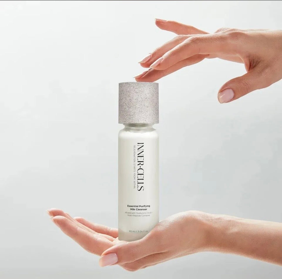 Hands holding Inner-Cells Essential Purifying Milk Cleanser bottle - lifestyle shot on light grey background